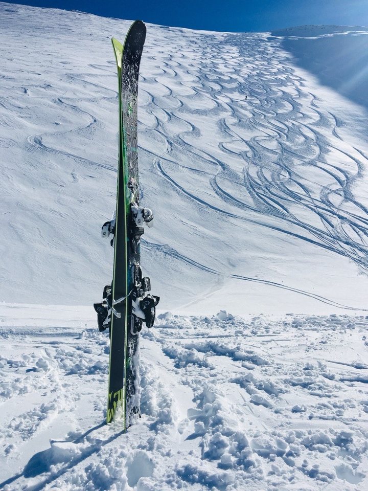 Skis planted in the snow above a slope already carved with tracks