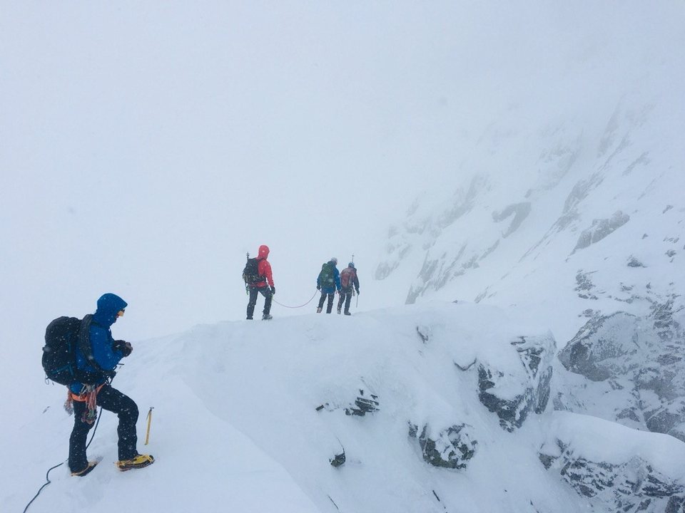 Moving along a snowy ridge in the mist, roped up and in crampons